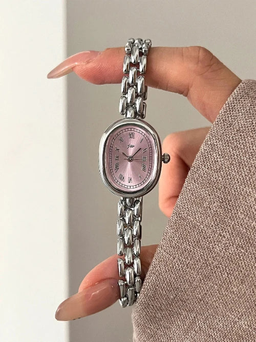 Hand holding a silver watch with a pink face against a neutral background
