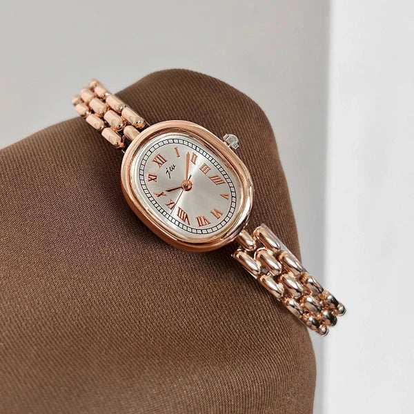 Rose gold watch with a white face on a brown cushion against a light gray background