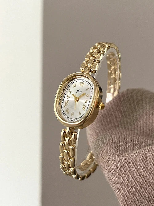 Gold wristwatch with a white face on a neutral background
