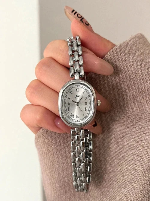 Silver watch with chain strap held by a hand against a neutral background